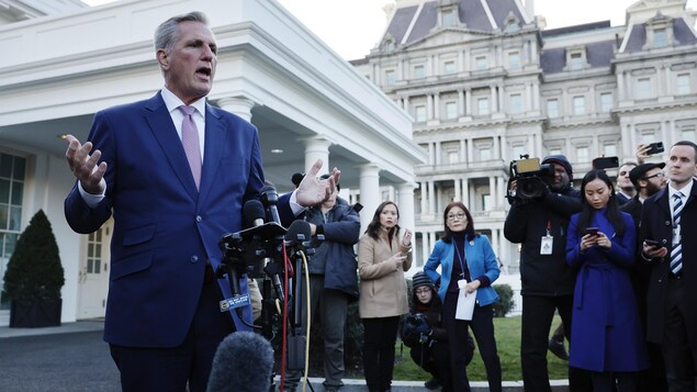 Un homme portant un veston bleu parle devant la Maison-Blanche. 