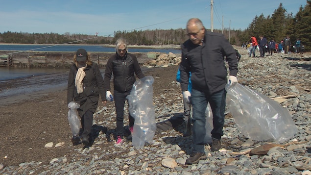 Catherine McKenna marche sur la plage avec d'autres gens en déposant des déchets dans de grands sacs Catherine McKenna marche sur la plage avec d'autres gens en déposant des déchets dans de grands sacs