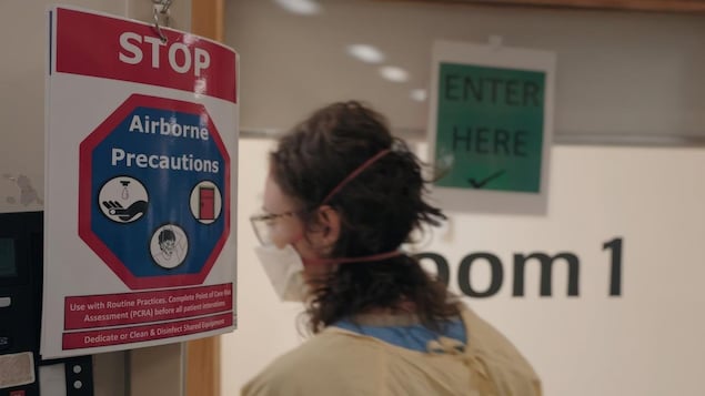 A healthcare worker wearing PPE next to a sign saying "STOP - Airborne - Precautions" with various instructions for both patients, visitors and personnel in a hospital.