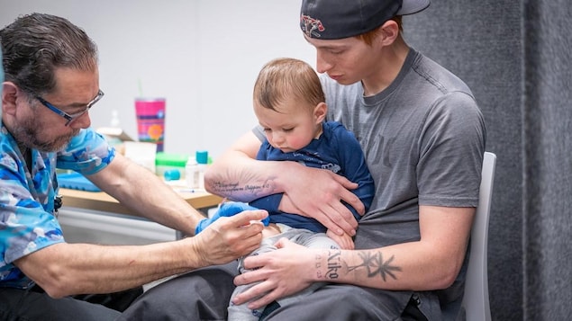 A healthcare provider gives a vaccine to a toddler being held by his father.