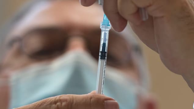 Un médecin manipule une seringue de vaccin.