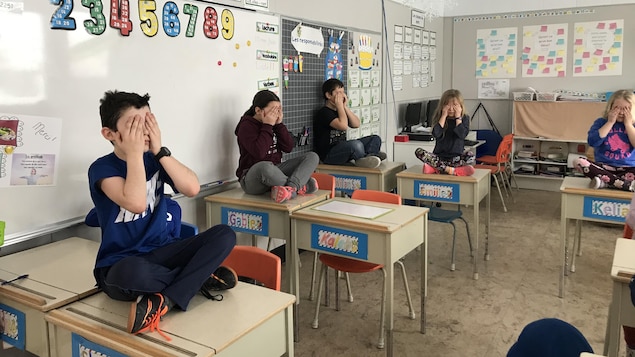 Des enfants sont assis sur leur pupitre, les mains sur les yeux, méditant.