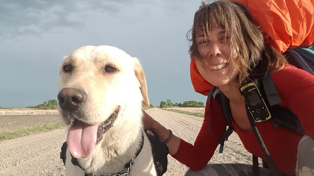 Melanie Vogel et son chien sont le long d'un chemin de terre et regardent l'objectif de l'appareil photo.