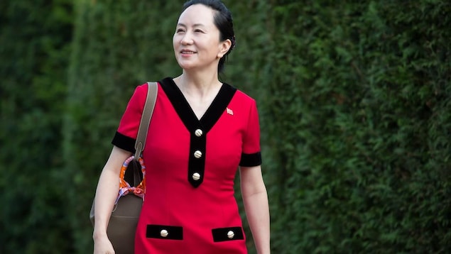 Meng Wanzhou souriante et portant une robe rouge devant un mur de cèdres.
