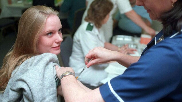 Une jeune femme lève les yeux vers une infirmière qui lui administre un vaccin.