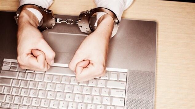 Deux mains menottées, poings fermés, sur un clavier d'ordinateur.