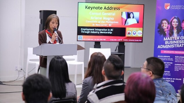 Isang babae nagsasalita sa podium sa harap ng mga estudyanteng Pilipino.