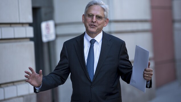 Merrick Garland, les bras ouverts, devant un immeuble.