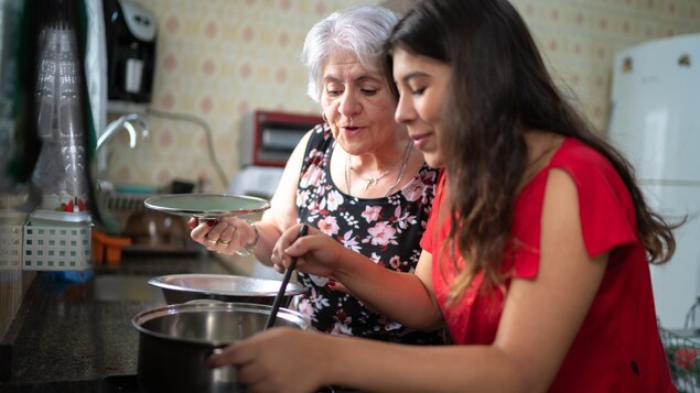 Deux femmes, dont une plus âgée, sont en train de cuisiner et regardent le contenu d'une marmite.