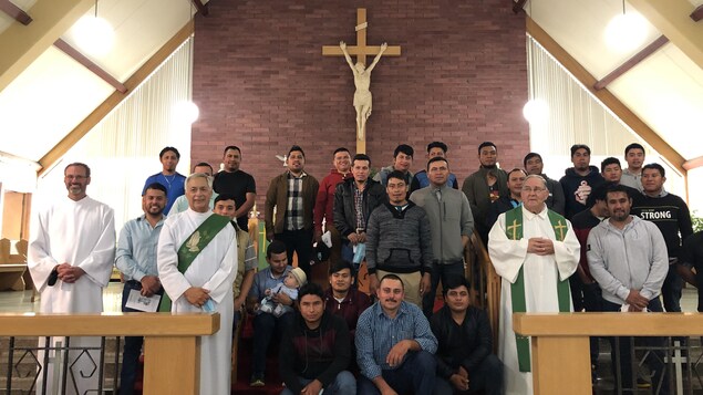 Une vingtaine de travailleurs saisonniers de l'industrie agricole dans une église avec trois célébrants.
