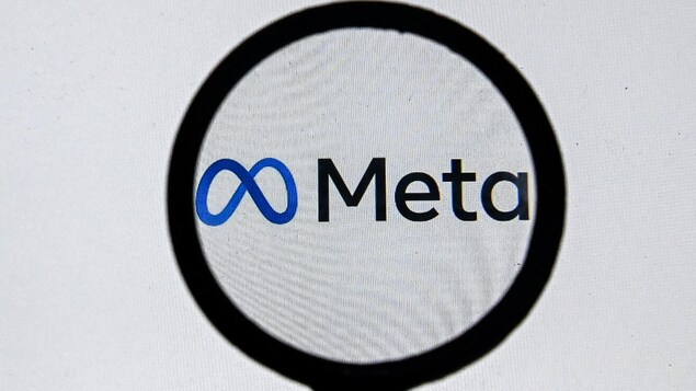 Le logo de Meta sur un écran d'ordinateur blanc vu à travers une loupe.