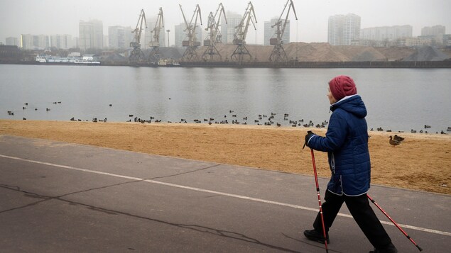 Une femme marche le long d'un cours d'eau à Moscou en plein hiver sans neige.