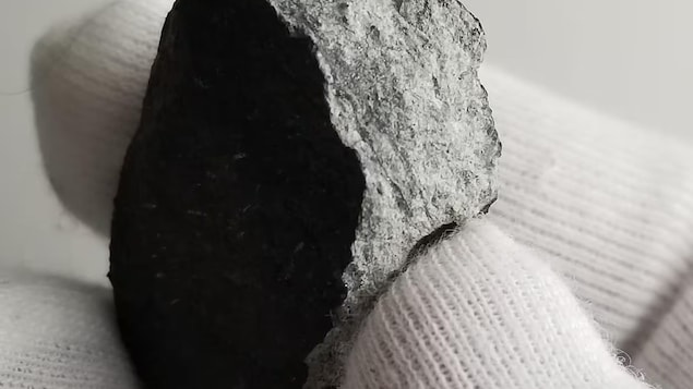 Una mano sostiene un fragmento de meteorito.