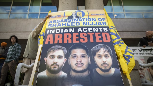 متظاهرون من أنصار الناشط الكندي السيخي المغدور هارديب سينغ نيجار يرفعون صورة للمتَّهمين الهنود الثلاثة كُتب عليها أنهم ’’عملاء هنود‘‘. 