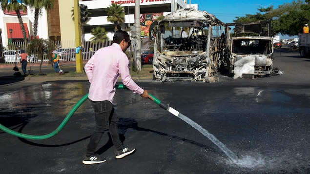 Un homme nettoie une rue dans la ville de Culiacan où des véhicules calcinés sont visibles.