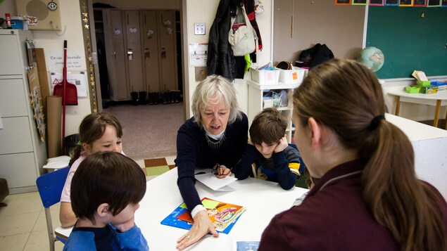 De jeunes élèves de la maternelle sont attablés autour d'une table basse couverte de contes, alors que l'aînée Suzanne Lavallée tourne la page d'un livre. De jeunes élèves de la maternelle sont attablés autour d'une table basse couverte de contes, alors que l'aînée Suzanne Lavallée tourne la page d'un livre.
