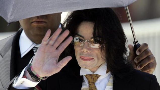Michael Jackson, qui porte des lunettes, tente de protéger son visage avec sa main.