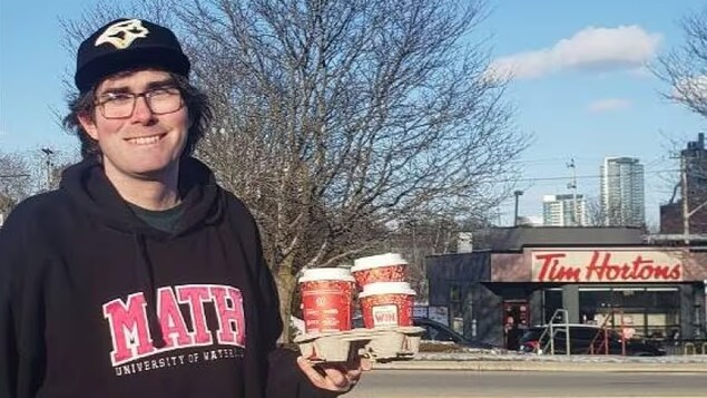 Michael Wallace avec des cafés à la main devant un Tim Hortons.