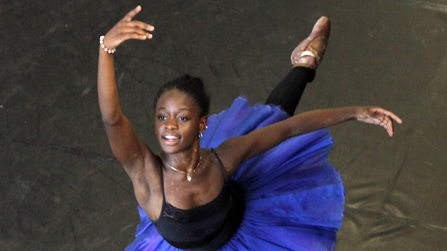 La danseuse Michaela DePrince, portant un tutu bleu et un haut noir, effectue une figure de danse, le bras droit et la jambe gauche levés. La danseuse Michaela DePrince, portant un tutu bleu et un haut noir, effectue une figure de danse, le bras droit et la jambe gauche levés.