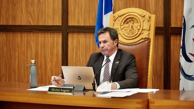 Michel Angers assis derrière la table du conseil municipal.