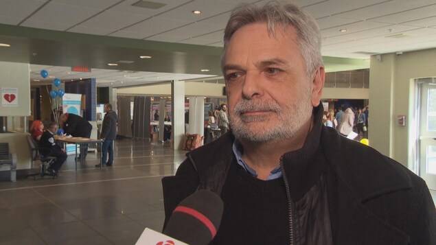 Un homme avec une barbe et un manteau dans un atrium en entrevue au micro de Radio-Canada. Un homme avec une barbe et un manteau dans un atrium en entrevue au micro de Radio-Canada.