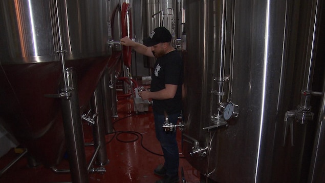 Un homme verse un verre de bière à partir d'une grande cuve dans une microbrasserie.