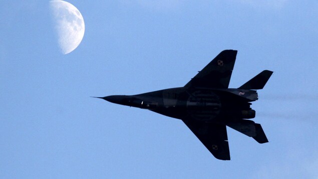 Un avion dans le ciel passe devant la lune.
