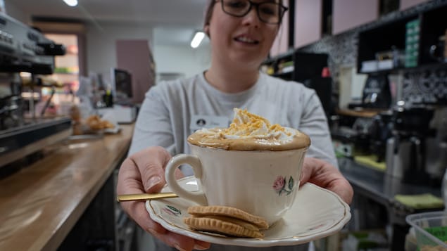 Une femme présente à bout de bras un café dans une tasse avec un biscuit à l'érable.