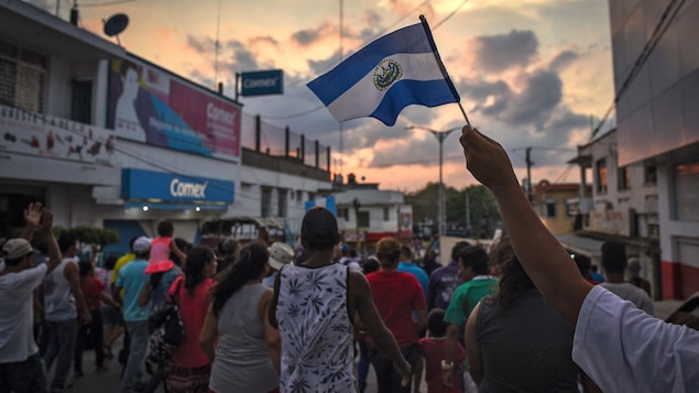 Des migrants marchent au soleil couchant, un drapeau guatémaltèque flotte dans les airs.