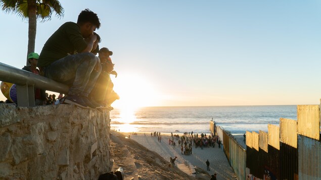 De jeunes hommes perchés sur un parapet regardent la mer et le mur qui les séparent des États-Unis.
