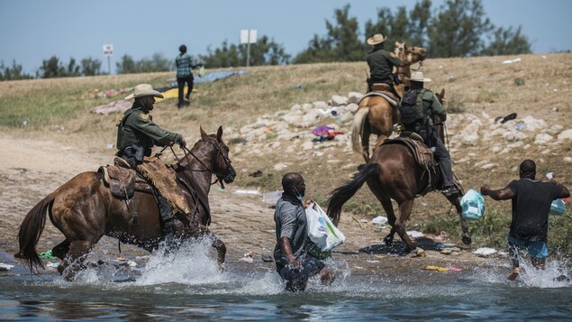 Des cavaliers américains sont dans le Rio Grande avec leurs chevaux et poursuivent des Haïtiens qui essaient de sortir de l'eau.