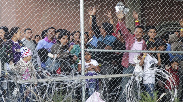 Des migrants font un signe de salutation avec la main derrière une grille. 