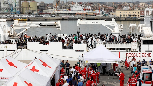 Un bateau transportant des centaines de migrants est amarré au port de Catane. Des dizaines de personnes attendent de descendre sur le pont; d'autres sont pris en charge par la Croix-Rouge après leur descente. Un bateau transportant des centaines de migrants est amarré au port de Catane. Des dizaines de personnes attendent de descendre sur le pont; d'autres sont pris en charge par la Croix-Rouge après leur descente.