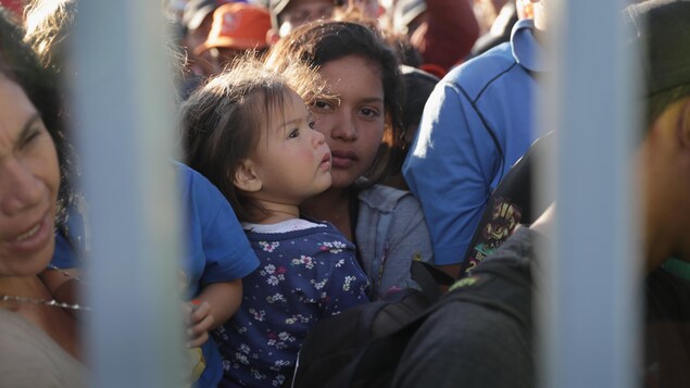 Des gens sont entassés derrière des barreaux, au centre de la photo, une jeune femme tient une enfant dans ses bras. Des gens sont entassés derrière des barreaux, au centre de la photo, une jeune femme tient une enfant dans ses bras.