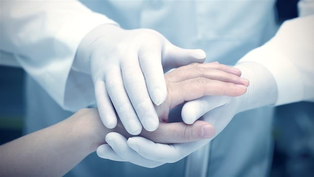 Des mains gantées tiennent une main non-gantée
