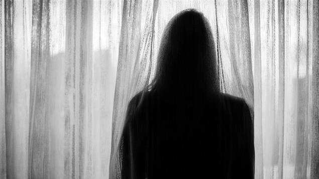 Une femme regarde à travers un rideau.