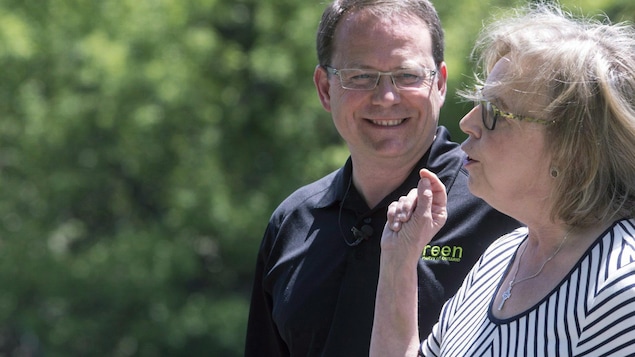 Mike Schreiner, portant un t-shirt noir, regarde Elizabeth May, vêtue d'une robe. Mike Schreiner, portant un t-shirt noir, regarde Elizabeth May, vêtue d'une robe.