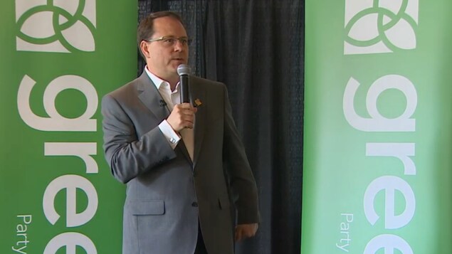 Mike Schreiner se tient sur une scène devant deux banderoles du Parti vert Mike Schreiner se tient sur une scène devant deux banderoles du Parti vert