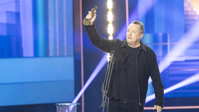 L'humoriste porte son trophée dans les airs sur scène. 