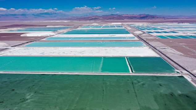 Des bassins de saumure et des zones de traitement d'une mine de lithium sont de couleur turquoise. À l'arrière-plan, il y a des montagnes.
