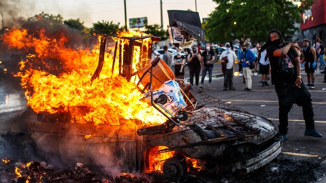 Des manifestants près d’une voiture en feu.