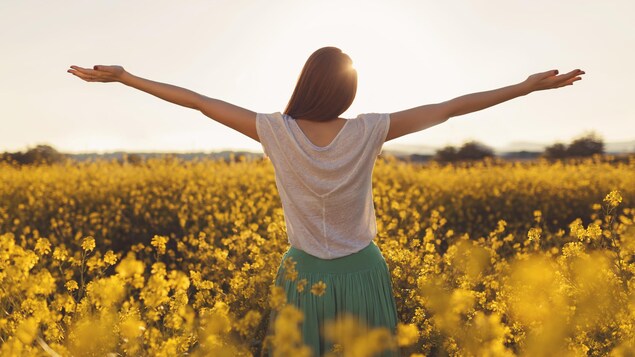 Femme profitant du soleil dans un champ de fleurs jaunes