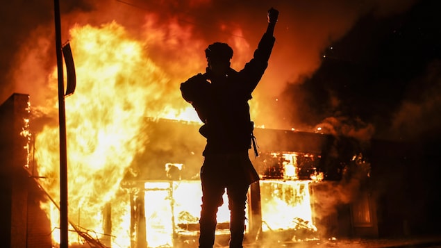 Un manifestant poing en l'air devant un édifice en feu.