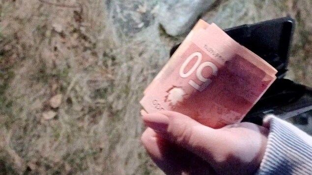 Une femme qui semble être dans un champ prend une photo de sa main qui tient des billets de 50 $.