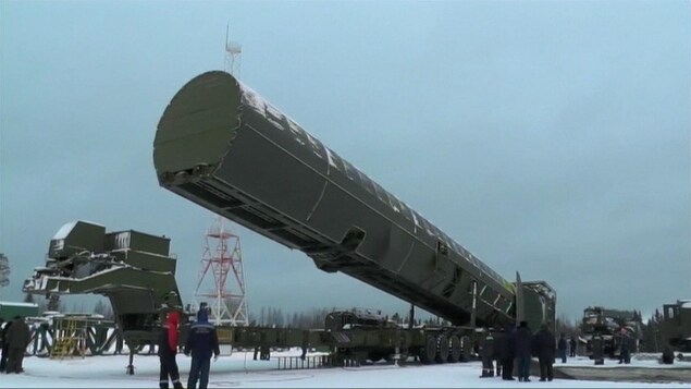 Le missile, dans un immense contenant de métal vert est transporté à l'extérieur sur un camion remorque sous le regard de personnes vêtues de manteau. Le missile, dans un immense contenant de métal vert est transporté à l'extérieur sur un camion remorque sous le regard de personnes vêtues de manteau.