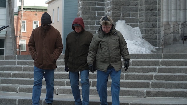 Trois hommes descendent les marches d'un parvis d'église, en hiver. 