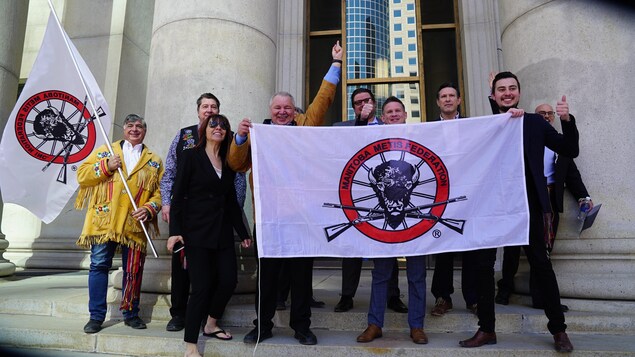 Un groupe de personnes qui sourient en tenant des drapeaux devant un bâtiment avec des colonnes.
