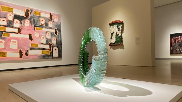 Au centre, une sculpture en forme de cercle, fait de bouteille vide d'alcool. À gauche, un tableau avec des rouleaux de papier de toilette et des cigarettes. À droite, une oeuvre avec le logo de la boisson gazeuse 7-Up. 