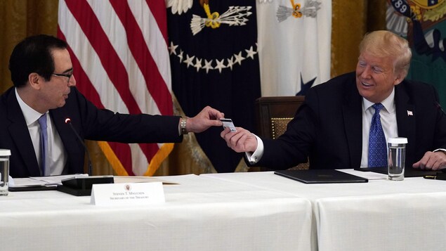 Donald Trump sourit à Steven Mnuchin, qui lui remet une carte de débit qui sera utilisée pour envoyer des paiements par le département du Trésor aux Américains lors d'une réunion de cabinet dans la salle Est de la Maison Blanche