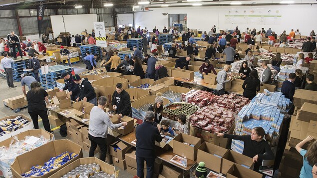 Plusieurs personnes devant d'énormes boîtes remplies de denrées.